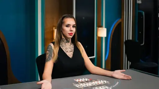 Krupiérka rozdávající karty při blackjacku v online kasinu. Krupiérka s tetováním před sebou na stole rozdává karty při hře blackjack.